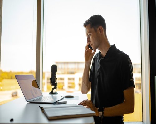 A person standing up while taking a phone call next to their office desk